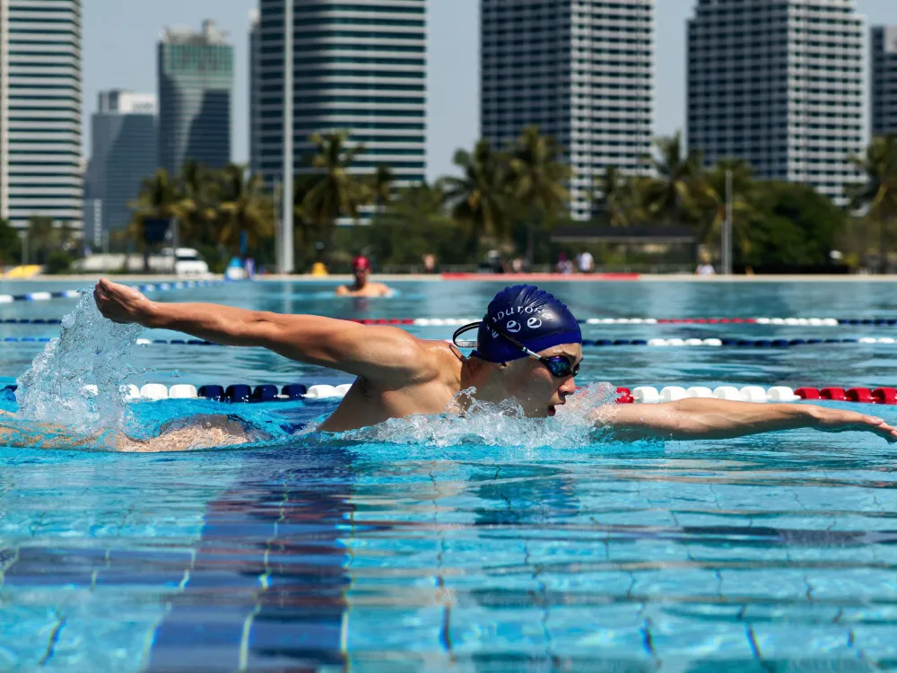 An adult swimmer refining their stroke technique in a Kuala Lumpur lap pool, the KL skyline behind.